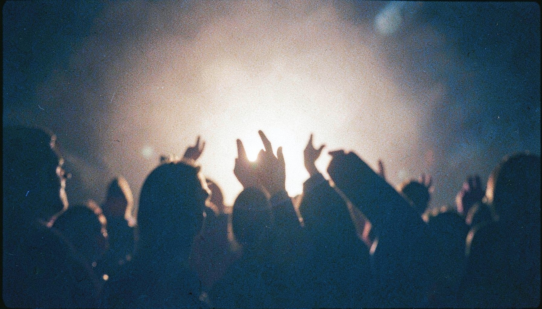 Analog film photograph of a praise and worship night, hands raised in silhouette against warm backlight, intimate and reverent mood with visible grain
